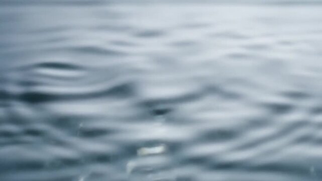 Ripples on Water Surface: Close-up view of gentle ripples spreading across a calm water surface, with a small droplet in focus, creating a serene and tranquil mood.