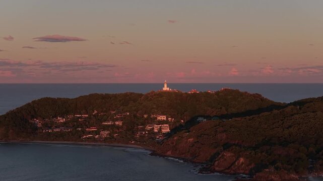Aerial view of Cape Byron Lighthouse at sunset, surrounded by lush vegetation and coastal cliffs in the Walgun Cape Byron State Conservation Area, Byron Bay, New South Wales, Australia.