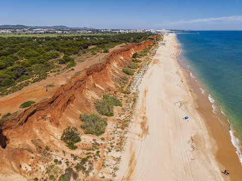 Aerial view of the red sandstone cliffs and sandy beach at Olhos de Agua in Olhos de Agua, Faro District, Portugal.