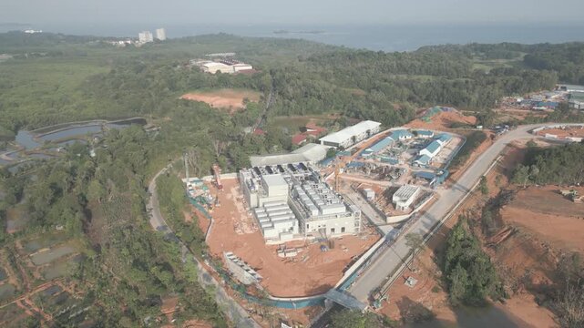 Aerial view of the Data Center Nongsa Batam construction site, featuring industrial buildings, surrounding lush greenery, and nearby coastal terrain in Batam, Riau Islands, Indonesia.