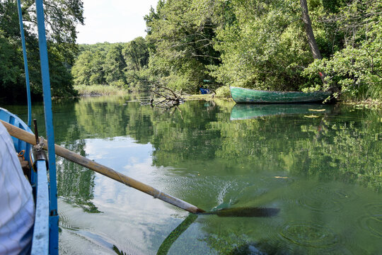 View of a wooden boat being rowed on the clear green waters of a river surrounded by lush trees and vegetation in Skopje, Greater Skopje, North Macedonia.