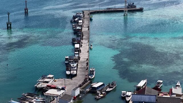 Aerial view of a long concrete pier with numerous boats docked in the clear turquoise waters in Karimunjawa, Central Java, Indonesia.