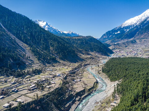 Aerial view of Ushu Forest and the Swat River flowing through the valley with terraced fields and snow-capped mountains in the background in Kalam, Khyber Pakhtunkhwa, Pakistan.