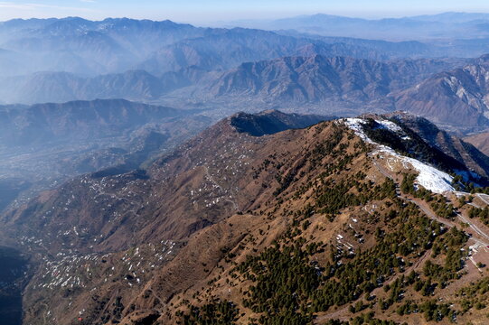 Aerial view of Pir Chinasi peak with snow-dusted slopes, pine forests, and a winding road overlooking the valley in Muzaffarabad, Azad Jammu Kashmir, Pakistan.