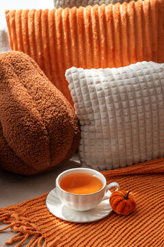 Autumn cozy scene with cup of tea and pumpkin decoration on textured blanket and pillows