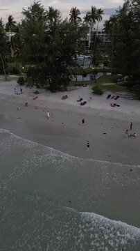 Aerial view of Lagoi Bay beach with palm trees, resort buildings, and people relaxing on the sand in Bintan, Riau Islands, Indonesia.
