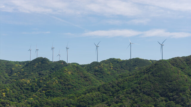 Aerial view of wind turbines situated on lush green hills under a clear blue sky in Japan.