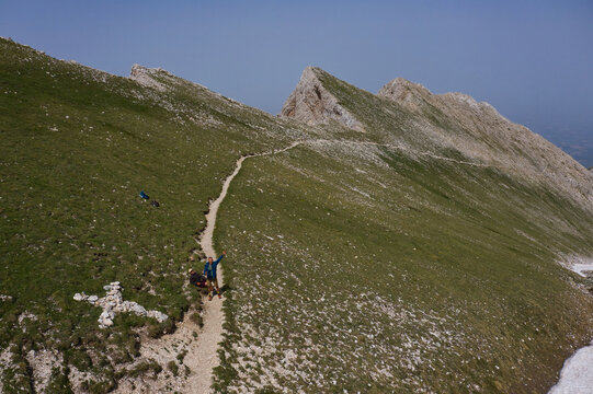 Aerial view of Monte Camicia with a hiking trail winding along the grassy mountain ridge, featuring two hikers on the path in Castelli, Abruzzo, Italy.