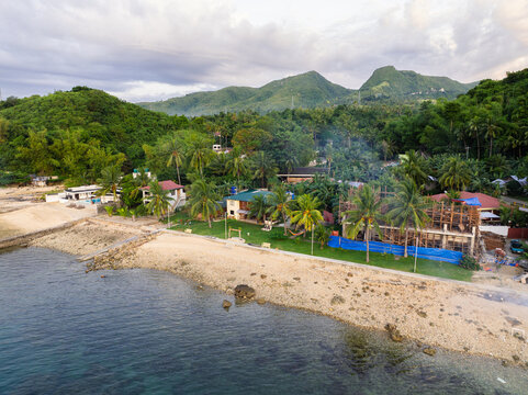 Aerial view of the coastal landscape along the Santander - Barili - Toledo Rd featuring palm trees, houses, and construction work near the beach in Alegria, Central Visayas, Philippines.
