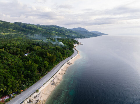 Aerial view of the Santander - Barili - Toledo Rd winding along the lush green coastline and sandy beach in Alegria, Central Visayas, Philippines.