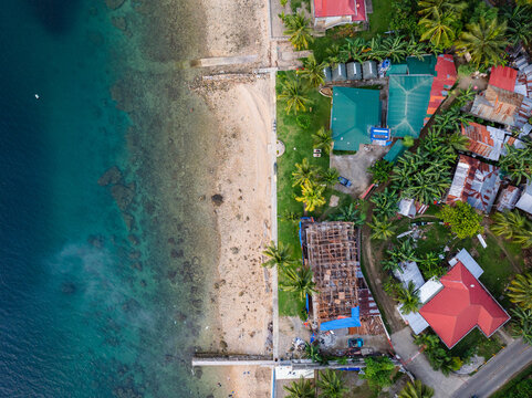 Aerial view of the coastal landscape along the Santander - Barili - Toledo Rd, featuring a sandy beach, turquoise waters, palm trees, and houses in Alegria, Central Visayas, Philippines.