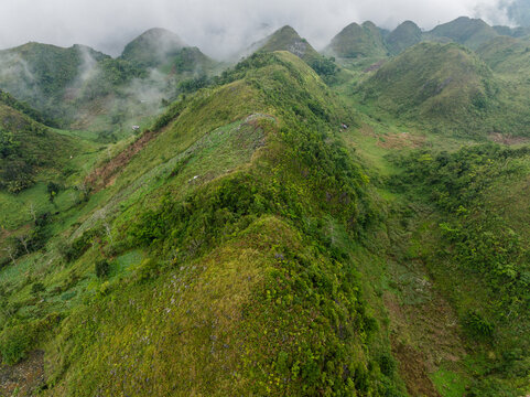 Aerial view of the lush green mountain ridges near Osmena Peak, featuring rolling hills covered in vegetation and mist in Dalaguete, Central Visayas, Philippines.