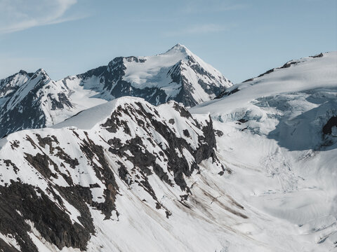 Aerial view of Byron Glacier featuring snow-covered mountain peaks, rugged rocky ridges, and glacial ice in Anchorage, Alaska, United States.