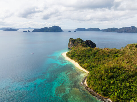Aerial view of Helicopter Island surrounded by lush tropical vegetation, a pristine sandy beach, and vibrant turquoise waters in Mimaropa, Philippines.