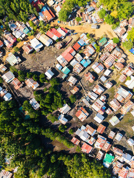 Aerial view of a residential neighborhood with houses featuring corrugated metal roofs, interspersed with lush trees and dirt paths in Puerto Princesa City, Mimaropa, Philippines.