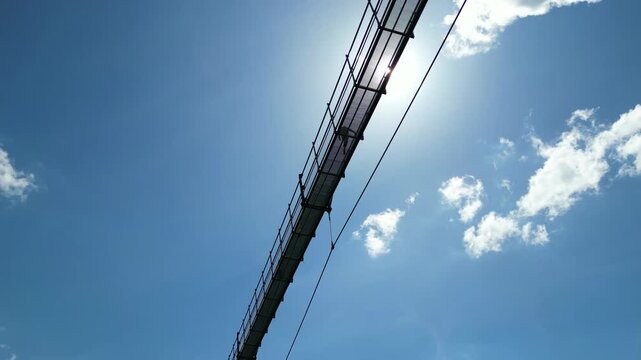 Aerial view of the Sky Bridge 721 suspension bridge spanning the valley with bright sunlight and blue sky in Dolni Morava, Pardubicky kraj, Czechia.