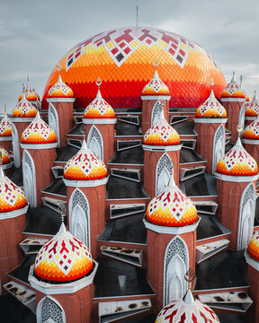 Aerial view of the Masjid Kubah 99 Asmaul Husna featuring vibrant orange and red patterned domes and intricate architectural details in Kecamatan Mariso, Sulawesi Selatan, Indonesia.