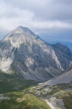 Aerial view of Campo Imperatore in the Apennine Mountains, featuring rugged rocky peaks, grassy slopes, and dramatic shadows under a cloudy sky in L'Aquila, Abruzzo, Italy.