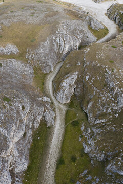 Aerial view of the rugged landscape of Campo Imperatore featuring a winding dirt path through limestone cliffs and grassy slopes in L'Aquila, Abruzzo, Italy.