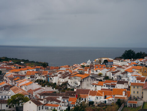 View of the historic city of Angra do Heroismo with its characteristic white buildings and orange tiled roofs overlooking the Atlantic Ocean in Angra do Heroismo, Azores, Portugal.