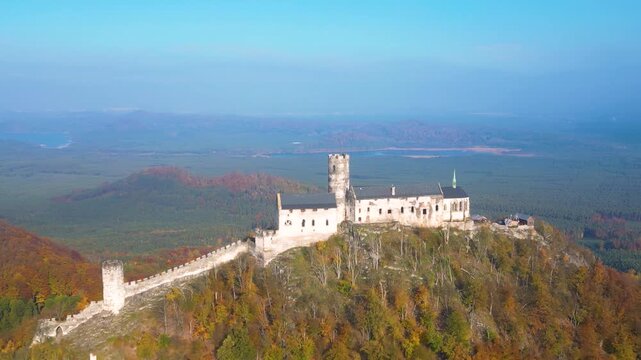 Aerial view of the historic State Castle Bezdez perched on a forested hilltop surrounded by autumn foliage under a clear blue sky in Bezdez, Liberecky kraj, Czechia.