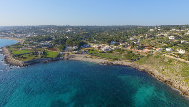 Aerial view of the coastline at Castrignano del Capo, featuring turquoise waters, rocky shores, green fields, and scattered buildings in Castrignano del Capo, Apulia, Italy.