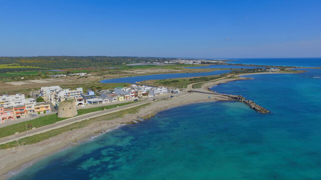 Aerial view of the historic Torre Mozza watchtower on the coast, surrounded by sandy beaches, turquoise sea, and coastal buildings in Torre Mozza, Apulia, Italy.