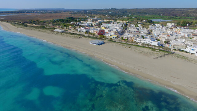 Aerial view of Torre Mozza beach with turquoise sea and white buildings along the coastline in Torre Mozza, Apulia, Italy.