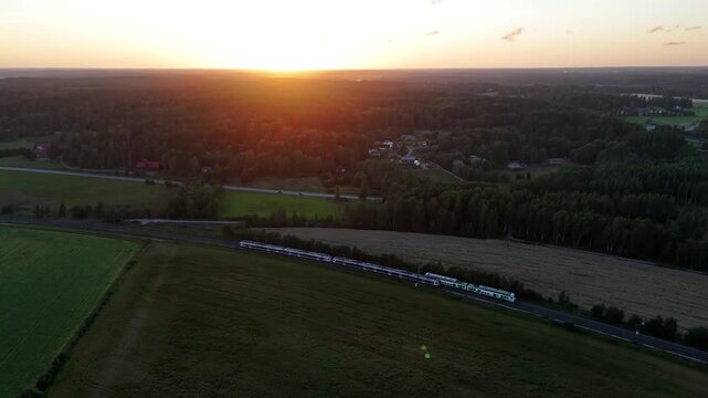 Aerial drone view of two passenger trains passing each other on parallel railway tracks at sunset surrounded by scenic forests and open countryside