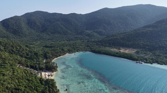 Aerial view of the turquoise waters and lush green hills of the Karimunjawa coastline in Karimunjawa, Central Java, Indonesia.