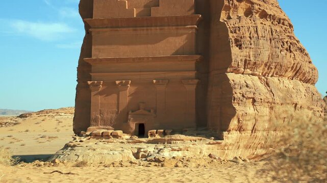 Lonely castle - largest tomb at Hegra archaeological site in Saudi Arabia Al Ula desert, camera moves up, calm hot day, only few shrubs moved by slow wind