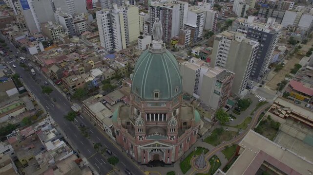 Aerial view of the Parroquia Inmaculado Corazon de Maria with its prominent green dome and statue, surrounded by urban buildings and streets in Magdalena del Mar, Lima Province, Peru.