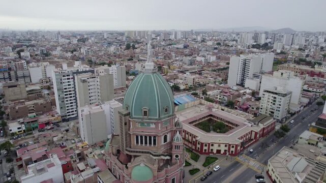 Aerial view of Inmaculado Corazon de Maria church with its distinctive green dome and pink facade surrounded by urban buildings and streets in Magdalena del Mar, Lima Province, Peru.