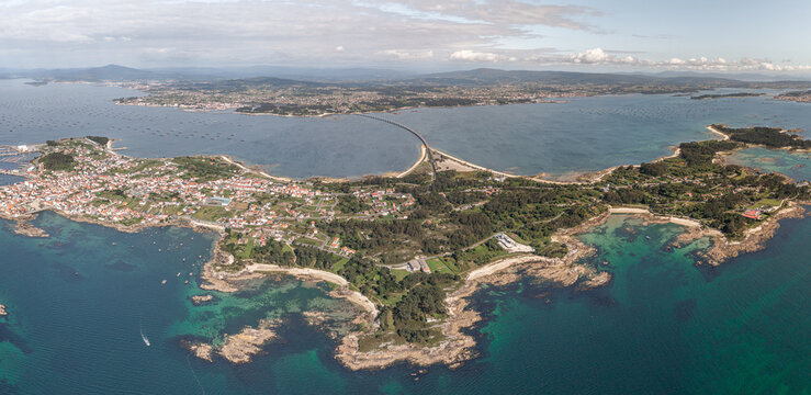 Aerial view of A Illa de Arousa, featuring the coastal town, the bridge connecting to the mainland, turquoise waters, rocky shorelines, and green landscapes in A Illa de Arousa, Pontevedra, Spain.