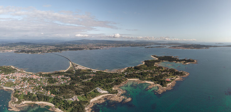 Aerial view of A Illa de Arousa showing the bridge connecting the island to the mainland, surrounded by blue waters, rocky coastlines, and lush greenery in A Illa de Arousa, Pontevedra, Spain.