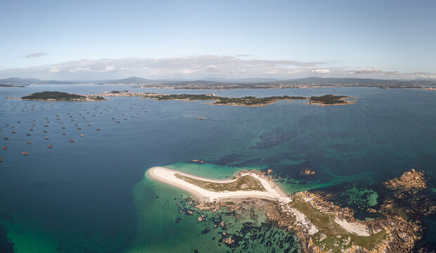 Aerial view of Illa do Areoso with white sandy beaches and turquoise waters surrounded by mussel rafts in Ria de Arousa, Pontevedra, Spain.