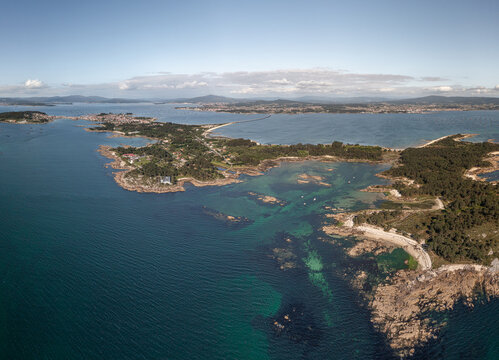 Aerial view of the coastline of A Illa de Arousa featuring rocky shores, turquoise waters, lush green vegetation, and the bridge in A Illa de Arousa, Pontevedra, Spain.