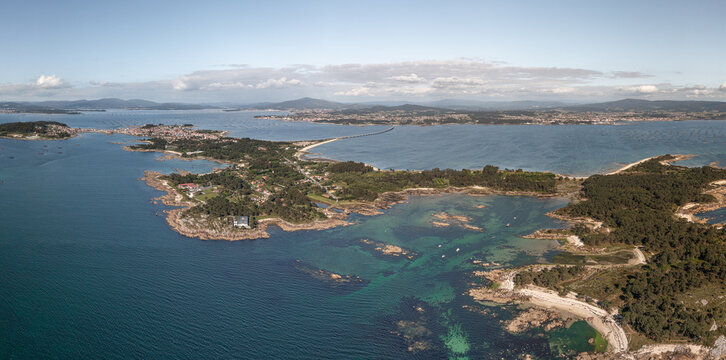 Aerial view of A Illa de Arousa featuring its rocky coastline, turquoise waters, and the bridge connecting the island to the mainland in A Illa de Arousa, Pontevedra, Spain.