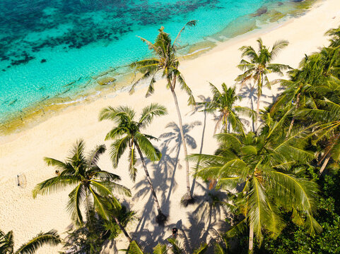 Aerial view of Puka Shell Beach in Boracay with white sand, turquoise water, and lush palm trees casting shadows on the beach in Malay, Western Visayas, Philippines.