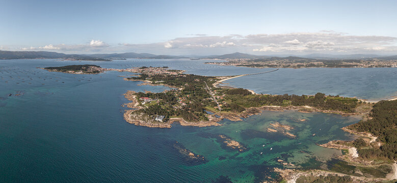 Aerial view of the coastal landscape of A Illa de Arousa, featuring turquoise waters, rocky shorelines, and the bridge connecting the island to the mainland in A Illa de Arousa, Pontevedra, Spain.