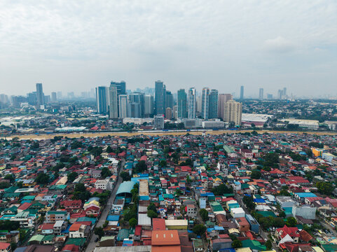 Aerial view of Eastwood City skyline rising above dense residential rooftops and urban sprawl in Pasig, Metro Manila, Philippines.