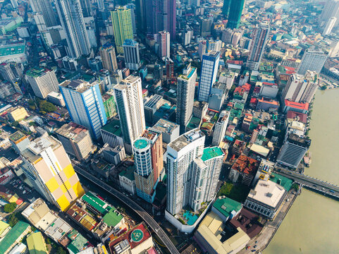 Aerial view of the dense urban skyline of Manila, featuring high-rise buildings, busy streets, and the Pasig River flowing through the city in Manila, Metro Manila, Philippines.