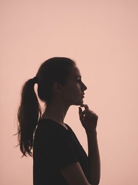 Silhouette of a thoughtful young woman with ponytail looking away against a soft pink glowing light background