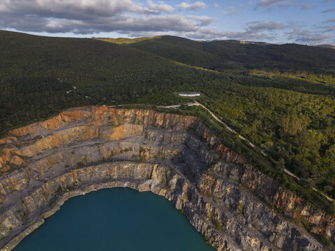 Aerial view of the Miradouro da Pedreira Azul featuring a deep turquoise quarry lake surrounded by rugged rock faces and lush green hills in Redinha, Leiria, Portugal.
