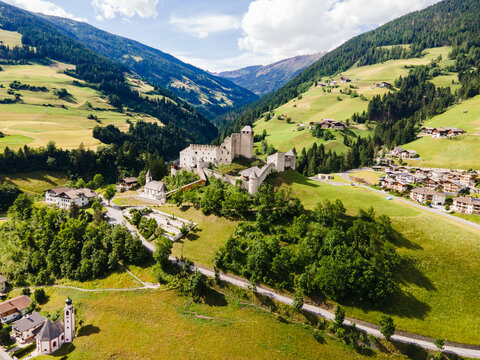 Aerial view of Burg Heinfels surrounded by lush green alpine meadows and the village of Heinfels in the Puster Valley, Heinfels, Tirol, Austria.