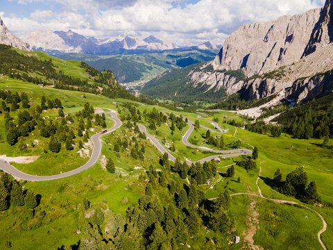 Aerial view of the winding road through the lush green meadows and rocky peaks of the Dolomites near Corvara, Trentino-Alto Adige, Italy.