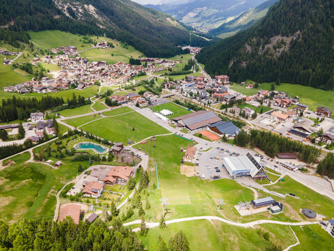 Aerial view of the alpine village of Corvara nestled in the green meadows of the Dolomites with ski lifts and mountain peaks in Corvara, Trentino-Alto Adige, Italy.