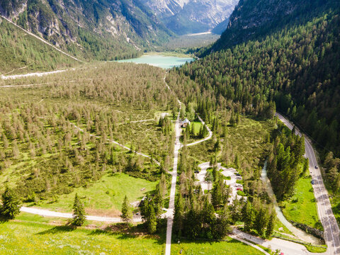 Aerial view of the Lunga Via delle Dolomiti trail winding through a pine forest near the turquoise Lago di Dobbiaco, surrounded by the Dolomites in Dobbiaco, Trentino-Alto Adige, Italy.