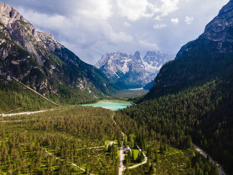 Aerial view of Lunga Via delle Dolomiti winding through the lush green forests and mountains near Lago di Dobbiaco, Dobbiaco, Trentino-Alto Adige, Italy.