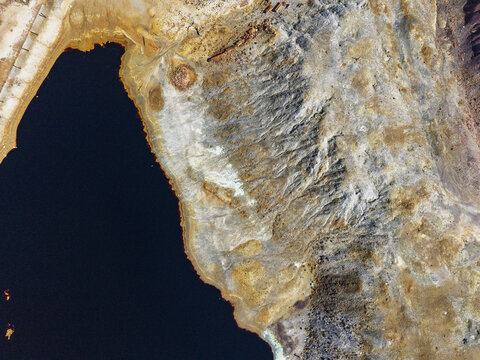 Aerial view of the mining landscape at Achada do Gamo featuring a dark acidic water reservoir and rugged terrain with mineral deposits in Achada do Gamo, Beja, Portugal.